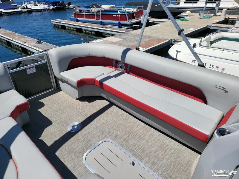 Slide: The Image of 2021 Bennington L25 Stern Radius pontoon boat interior with red and gray seating at marina. - 14