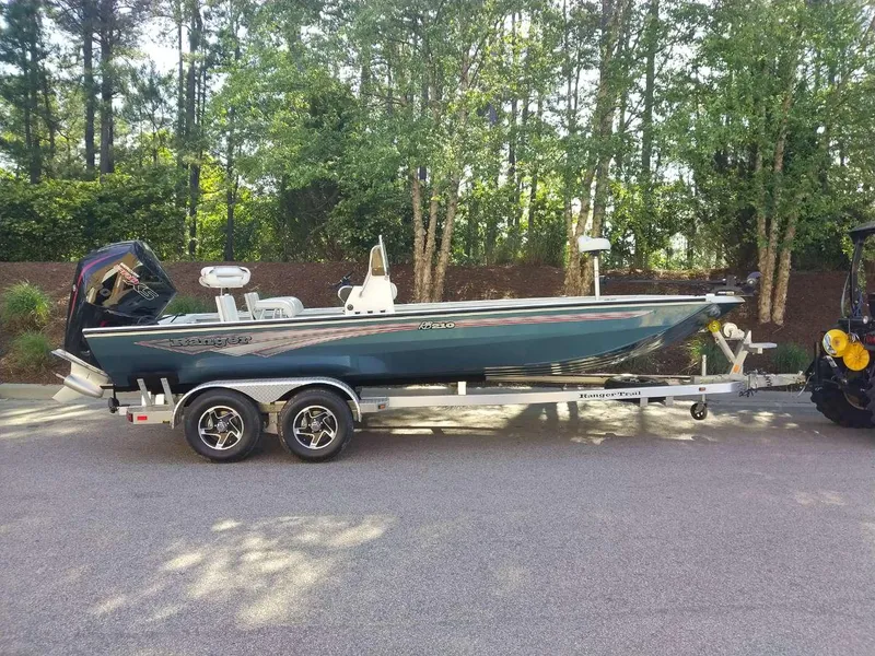 The Image of 2024 Ranger RB210 boat on a trailer, parked outdoors with trees in the background. - 0