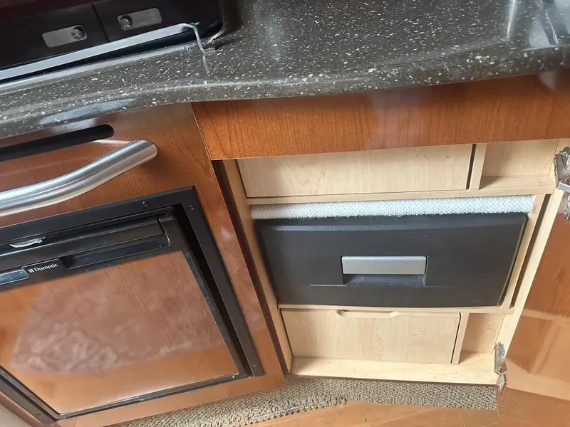 Slide: The Image of Kitchen area of 2012 Sea Ray 330 Sundancer with wooden cabinetry and compact fridge. - 24