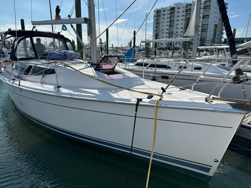 The Image of 2014 Hunter 33 sailboat docked at marina with modern buildings in background. - 0