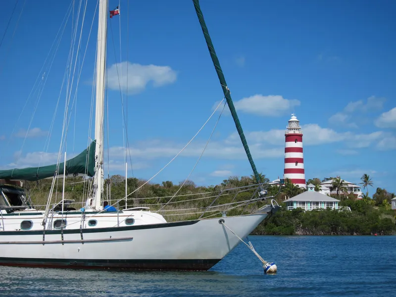 Slide: The Image of 1988 Pacific Seacraft Cutter sailboat anchored near a striped lighthouse under a clear blue sky. - 0