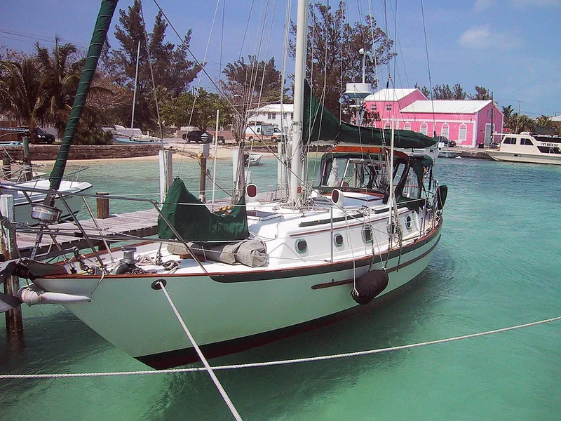 Slide: The Image of 1988 Pacific Seacraft Cutter sailboat docked in turquoise waters, with a pink building nearby. - 1