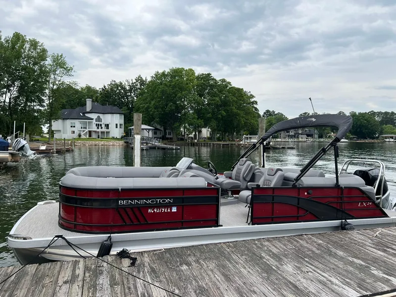 Slide: The Image of 2022 Bennington 24 LXFB pontoon boat docked by a scenic lakeside. - 0