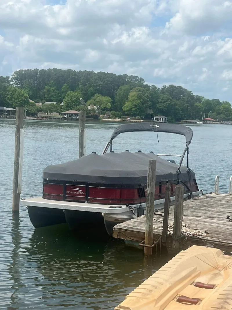 Slide: The Image of 2022 Bennington 24 LXFB pontoon boat docked on a serene lake. - 1