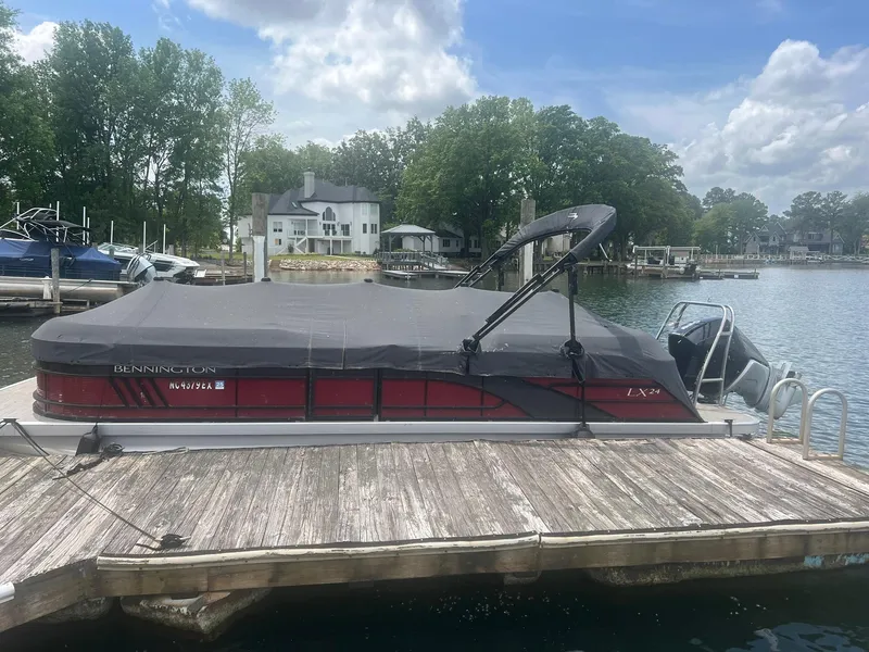 Slide: The Image of 2022 Bennington 24 LXFB pontoon boat docked at a lakeside marina. - 2