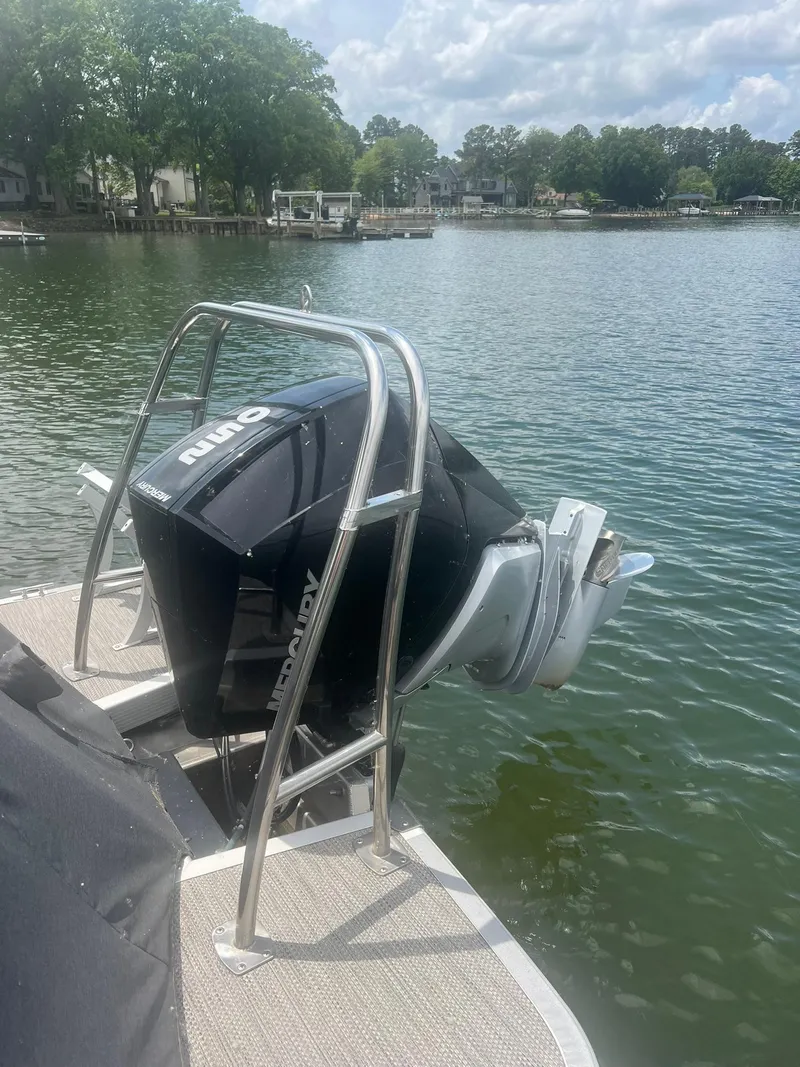 Slide: The Image of 2022 Bennington 24 LXFB pontoon boat with a black outboard motor on a lake. - 5