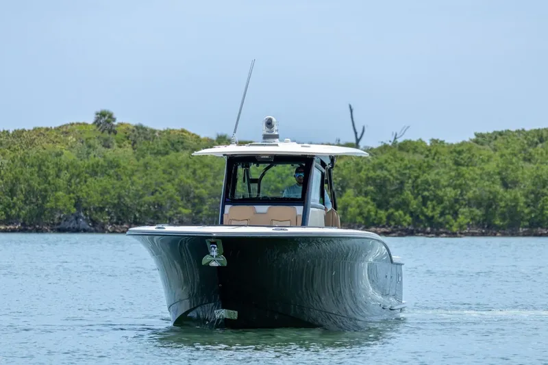 Slide: The Image of 2022 Scout 330 LXF boat cruising on calm water near lush green shoreline. - 2