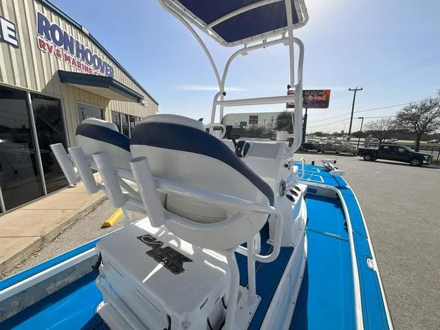 Slide: The Image of 2024 Majek 25 ILLUSION boat with blue and white seating, parked outside dealership. - 16