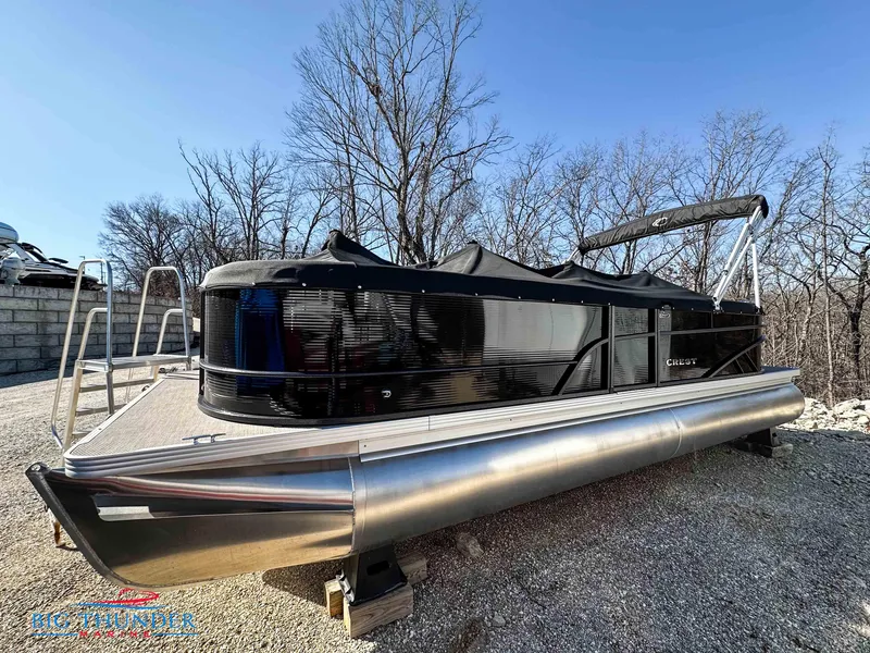Slide: The Image of 2023 Crest CLASSIC LX 240 SLC pontoon boat on gravel, surrounded by trees. - 0