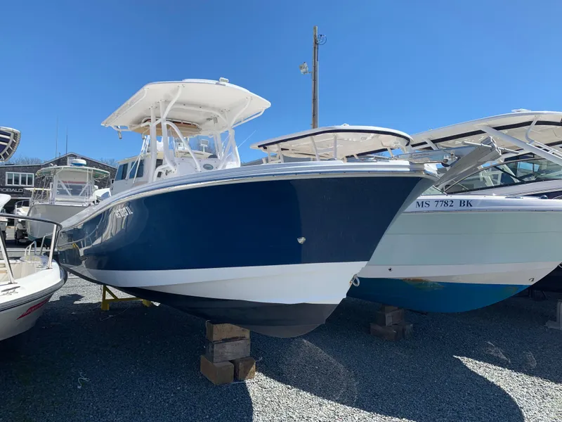 Slide: The Image of 2017 Edgewater 245 CC boat in a marina, blue and white hull, on wooden blocks. - 2