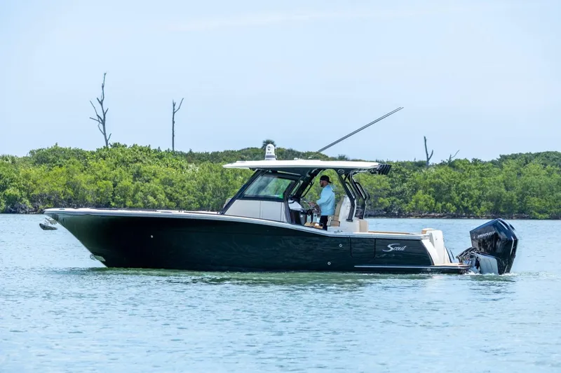 Slide: The Image of 2022 Scout 330 LXF boat cruising on calm water near lush greenery. - 0