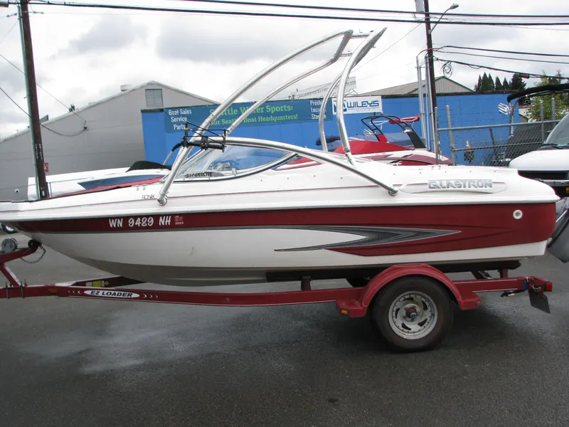 The Image of 1999 Glastron 175SX boat on a red trailer in a parking lot. - 0