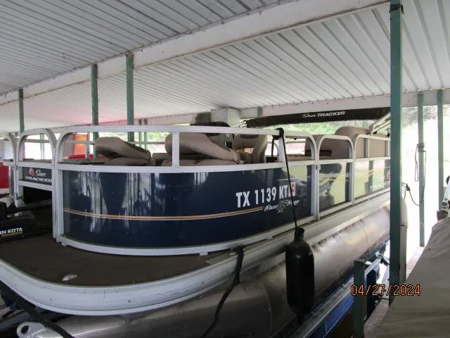 Slide: The Image of 2022 Sun Tracker Bass Buggy pontoon boat docked under a covered area. - 3