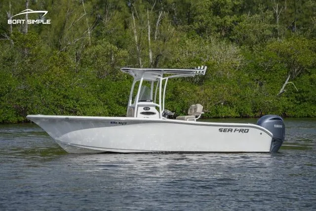Slide: The Image of 2023 Sea Pro 219 Deep V CC boat on calm water with lush greenery in the background. - 0