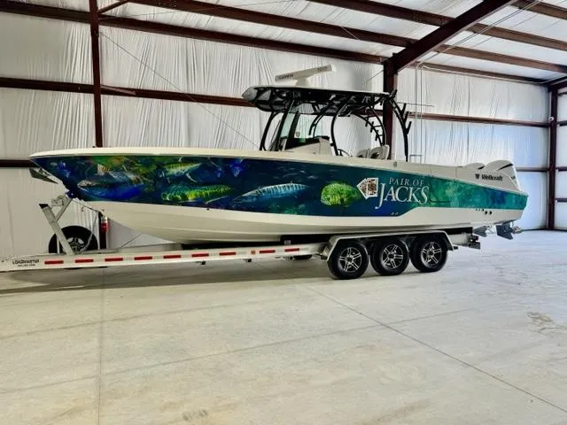 Slide: The Image of 2020 Wellcraft 302 Fisherman boat on trailer in warehouse, Pair of Jacks graphic on side. - 2