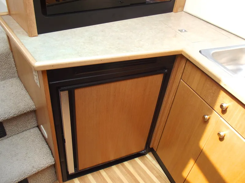 Slide: The Image of Bayliner 3388 Motor Yacht 2000 interior kitchen with wood cabinetry and compact refrigerator. - 21