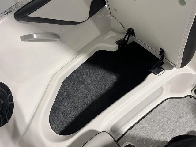 Slide: The Image of 2024 Yamaha Boats SX195 storage compartment with black carpet lining. - 27