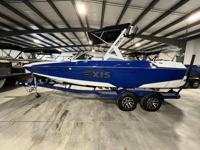 Slide: The Image of 2023 Axis Wake Research A20 boat in blue, displayed indoors on a trailer. - 1