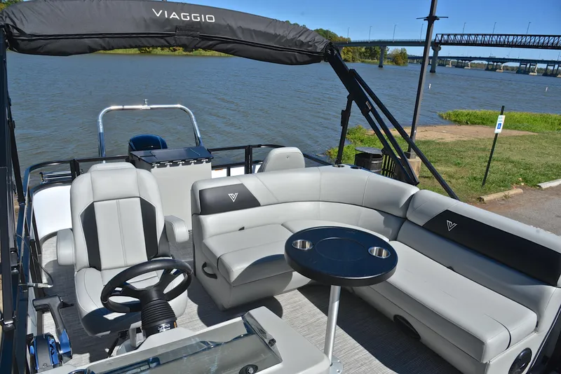 Slide: The Image of 2023 Viaggio DM18F pontoon boat interior with gray seating and table on a lake. - 20