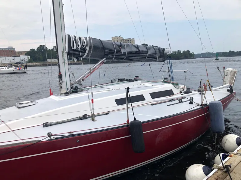 Slide: The Image of Red 1991 Tripp 36 sailboat docked on a calm river with buildings in the background. - 4