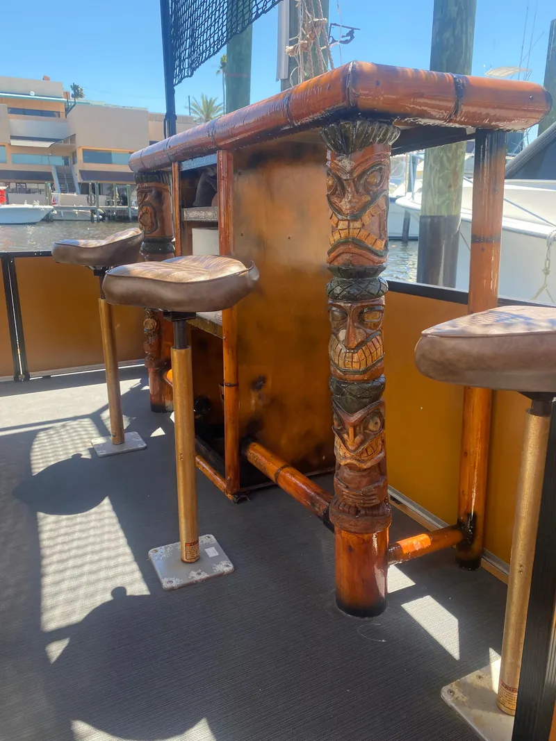 Slide: The Image of Custom 2024 Tiki Bahama Mama 1.0 bar with carved wooden stools on a boat dock. - 6