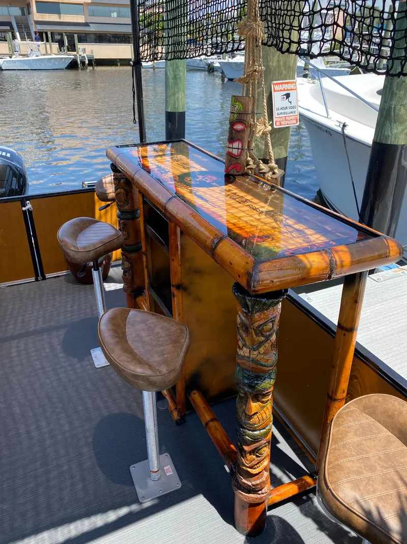 Slide: The Image of Tiki-themed boat bar with stools, Custom Tiki Bahama Mama 1.0, 2024 model, docked by the water. - 8