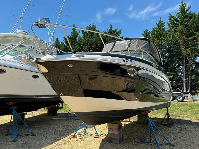 Slide: The Image of 2020 Crownline 264CR boat on stands, outdoors, sunny day, surrounded by trees. - 2