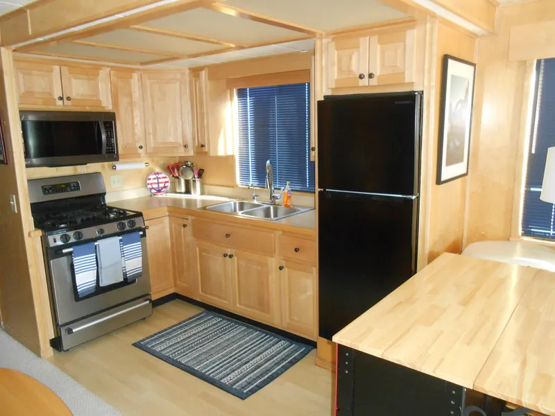 Slide: The Image of 2001 Stardust Cruisers houseboat kitchen with wooden cabinets, stainless steel appliances, and black refrigerator. - 6