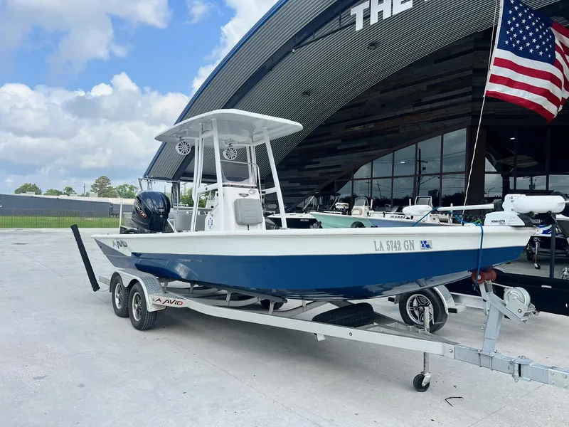 Slide: The Image of 2022 Avid 23 Mag boat on trailer, parked outside dealership with American flag. - 5