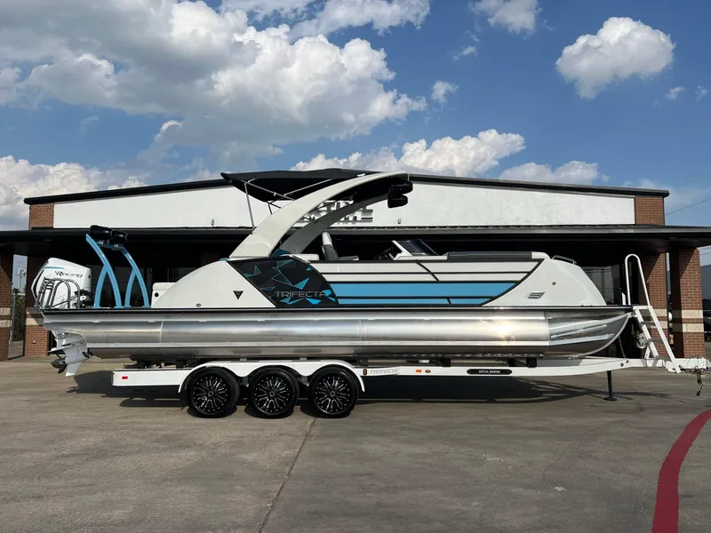 Slide: The Image of 2024 Trifecta 25 SPORT RL9 DC 3PLUS ARCH pontoon boat on trailer, parked outdoors. - 2