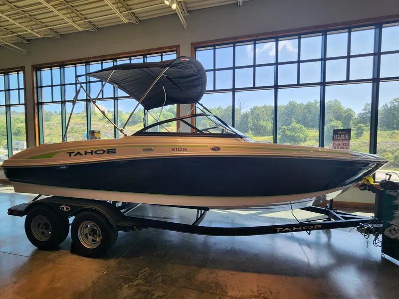 The Image of 2024 Tahoe 210 Si boat displayed indoors with a trailer, large windows in the background. - 0
