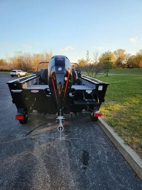 Slide: The Image of 2024 Tracker Targa V-18 WT boat parked on a paved area near grass. - 4