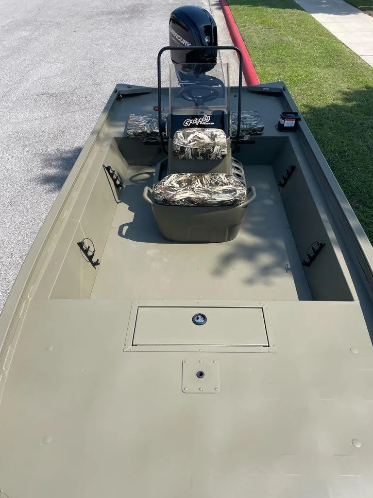 Slide: The Image of 2024 Tracker Grizzly 1860 CC boat with camouflage seats, parked on a street. - 2