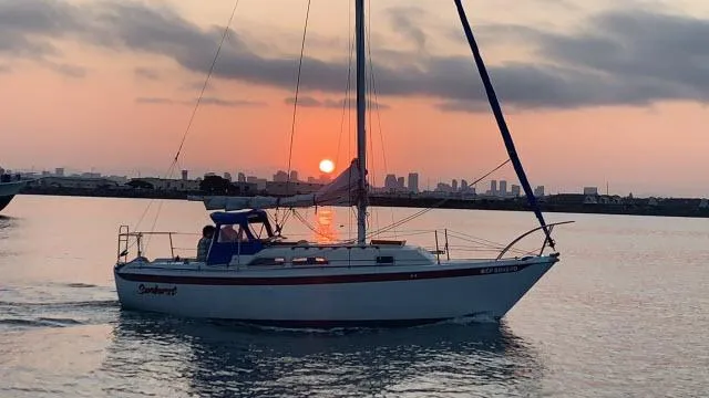 Slide: The Image of 1973 Ericson 27 sailboat cruising at sunset with city skyline in the background. - 1