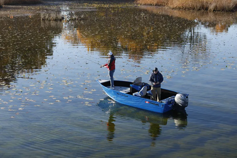 Slide: The Image of 2025 Smoker Craft Lazer 161 side console boat on a calm lake, two people fishing. - 21