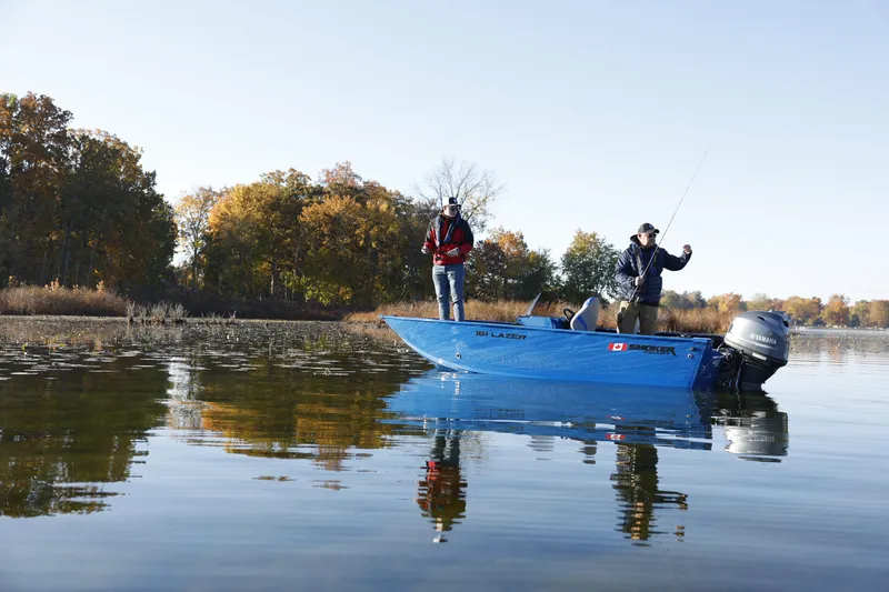 Slide: The Image of 2025 Smoker Craft Lazer 161 side console boat on a serene lake with autumn trees. - 22
