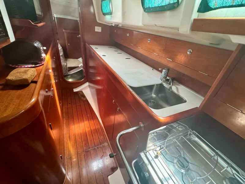 Slide: The Image of Interior of 1996 Beneteau Oceanis 40 CC yacht, featuring wooden cabinetry and compact kitchen area. - 14