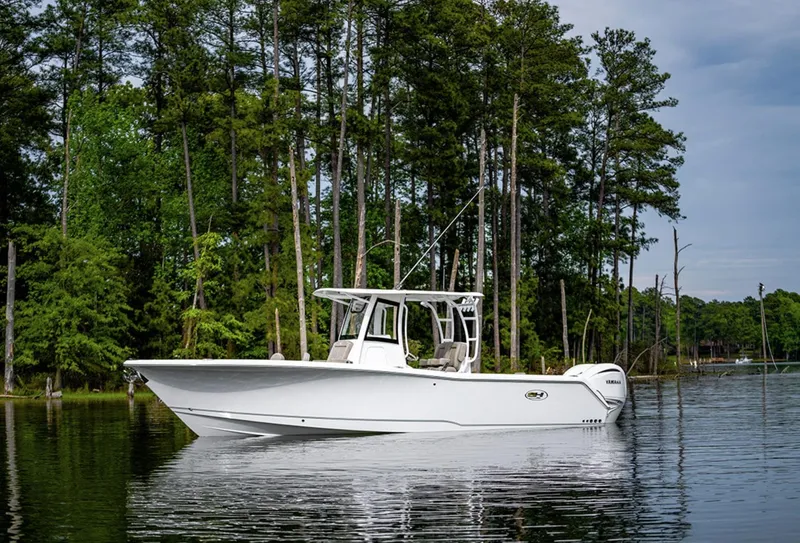 Slide: The Image of 2025 Sea Hunt GAMEFISH 28 boat on a serene lake with forest background. - 2