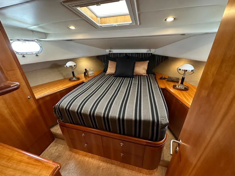 Slide: The Image of 1999 Queenship Cockpit Motoryacht bedroom with striped bedding, wooden cabinetry, and modern lighting. - 31