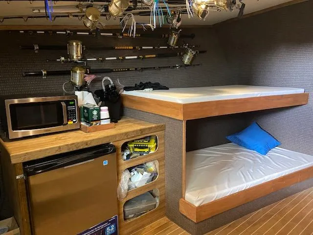 Slide: The Image of 2022 Custom Carolina Sportfish interior with bunk beds, fishing rods, microwave, and mini-fridge. - 13