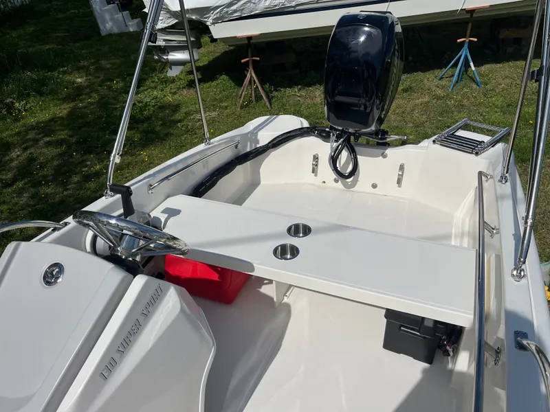 Slide: The Image of 2025 Boston Whaler 130 Super Sport boat interior with motor, cup holders, and seating. - 12