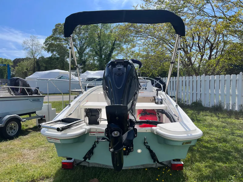 Slide: The Image of 2025 Boston Whaler 130 Super Sport boat with outboard motor, parked on grass. - 16