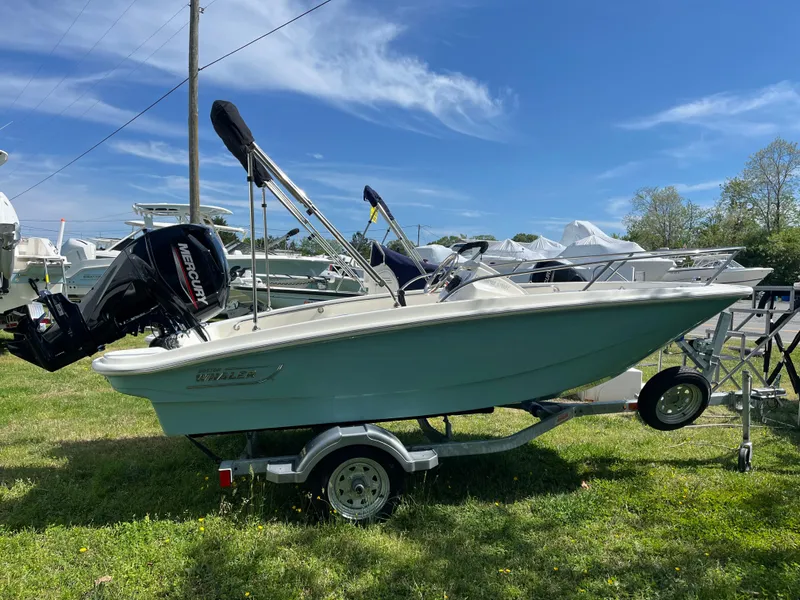 Slide: The Image of 2025 Boston Whaler 130 Super Sport boat on trailer, parked on grass under clear blue sky. - 18
