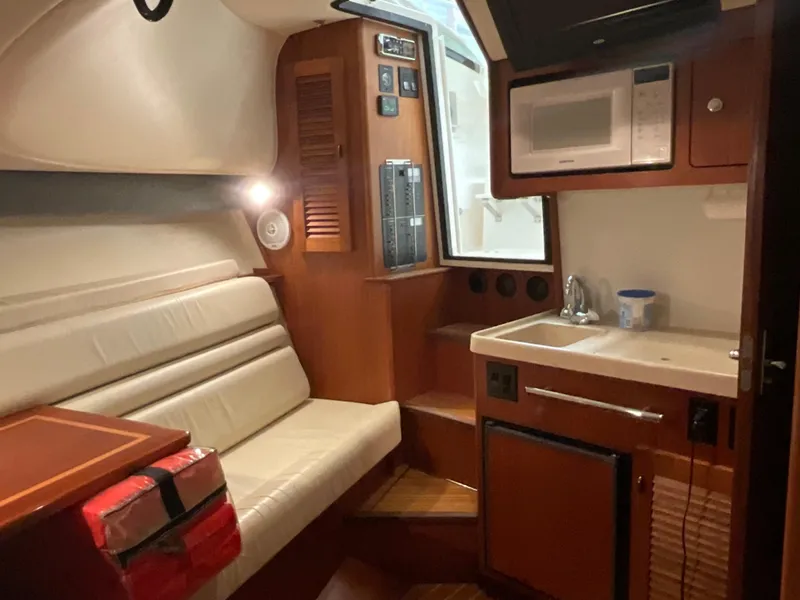 Slide: The Image of 1999 Pursuit Offshore Express cabin with seating, kitchenette, and microwave. - 15