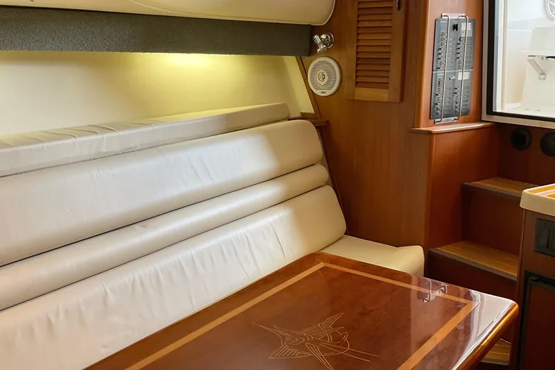 Slide: The Image of 1999 Pursuit Offshore Express cabin interior with white seating and wooden table. - 21