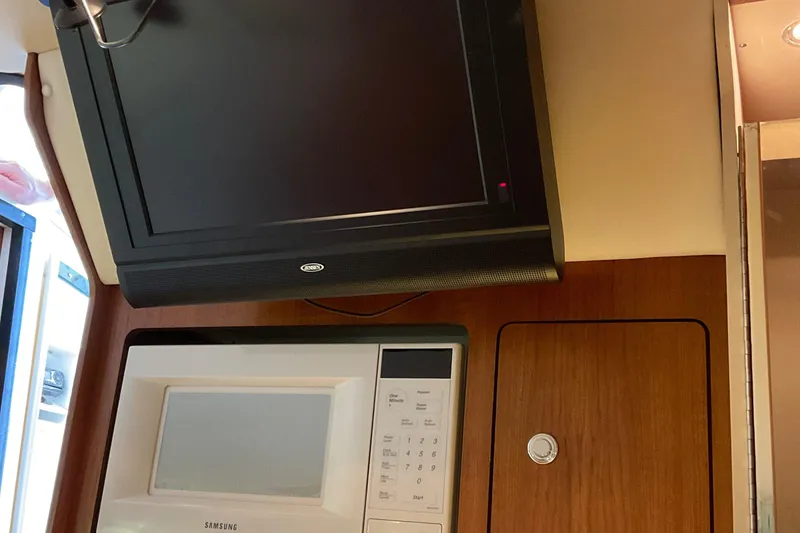 Slide: The Image of 1999 Pursuit Offshore Express interior with TV and microwave in wooden cabinetry. - 24