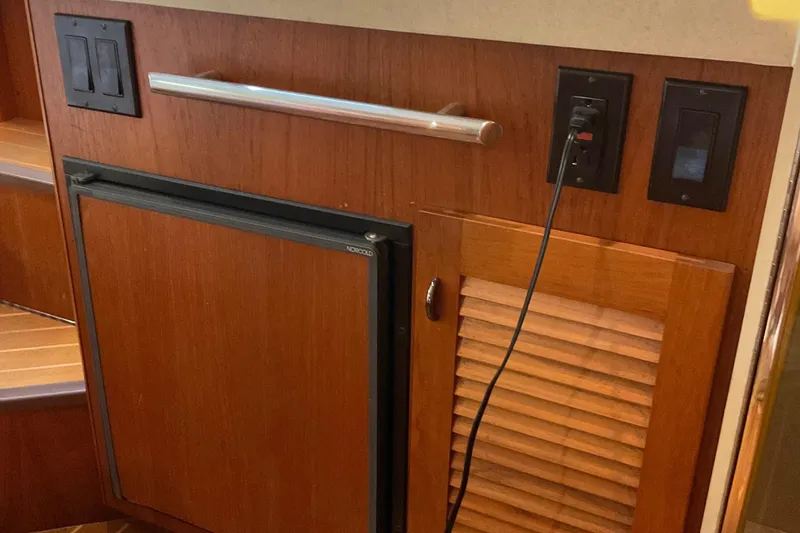 Slide: The Image of 1999 Pursuit Offshore Express interior with wooden paneling, mini fridge, and electrical outlets. - 25