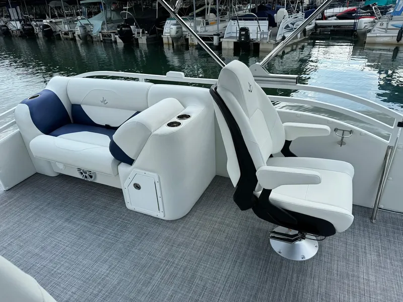Slide: The Image of 2024 JC Spirit Super Sport 24TT DSL boat interior with white and blue seating at marina. - 12