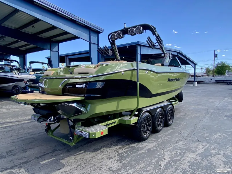 Slide: The Image of 2022 MasterCraft X26 boat in green, parked on a trailer at a marina. - 2
