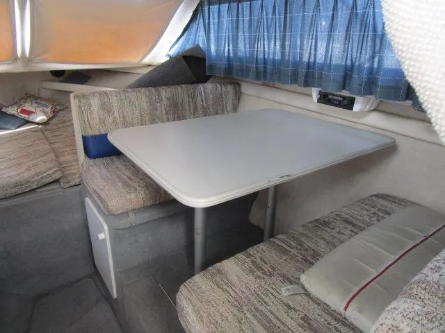Slide: The Image of Interior dining area of a 1994 Bayliner 2452 Classic boat with table and cushioned seating. - 13